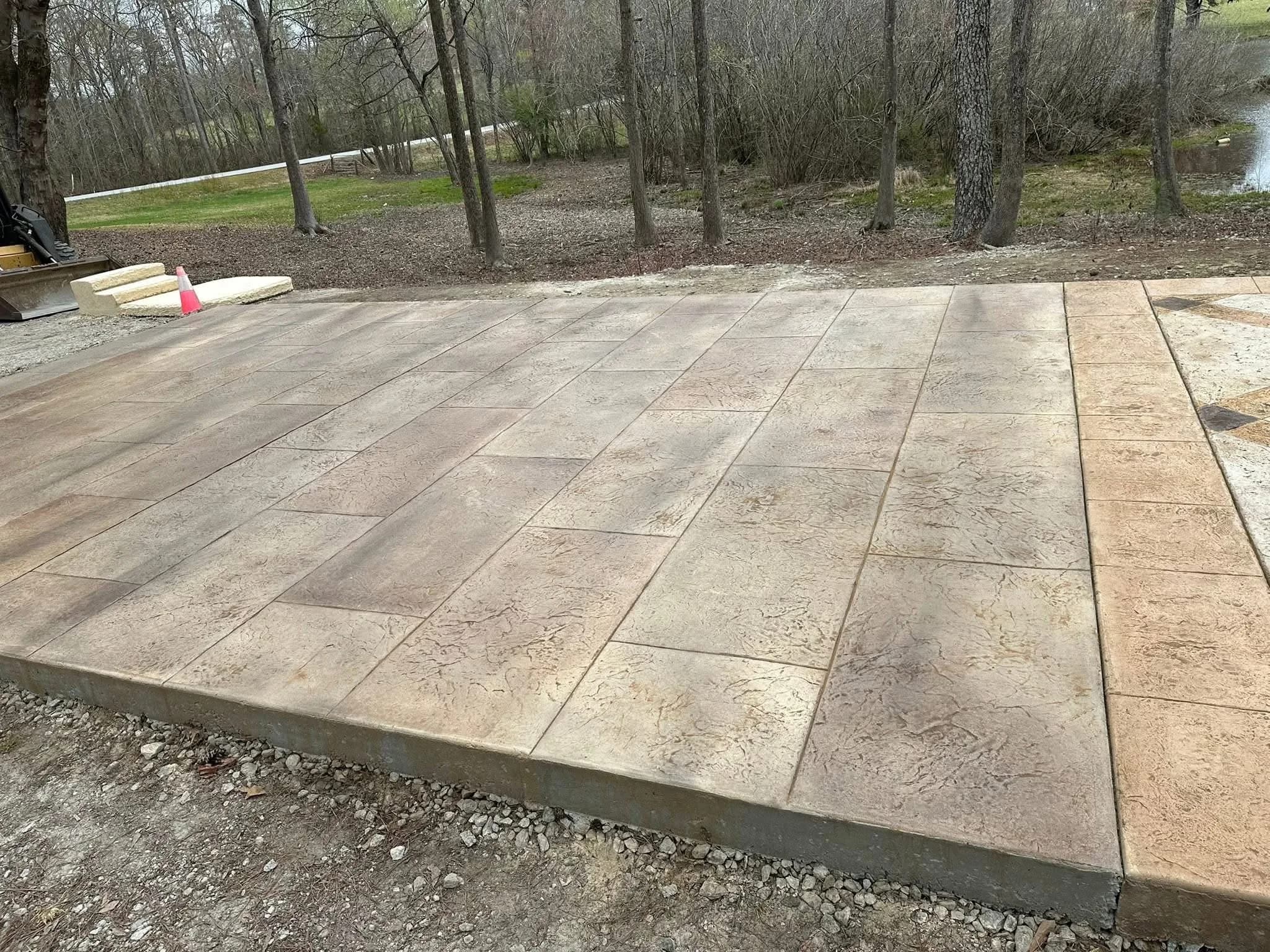 Stamped concrete patio with ashlar slate pattern in tan and brown, finished with a smooth troweled border, on a wooded property