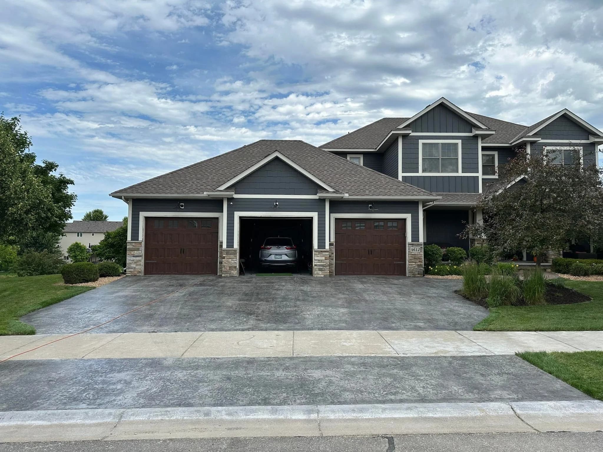 Wide three-car concrete driveway with control joints leading to a craftsman-style home in Albertville, Minnesota